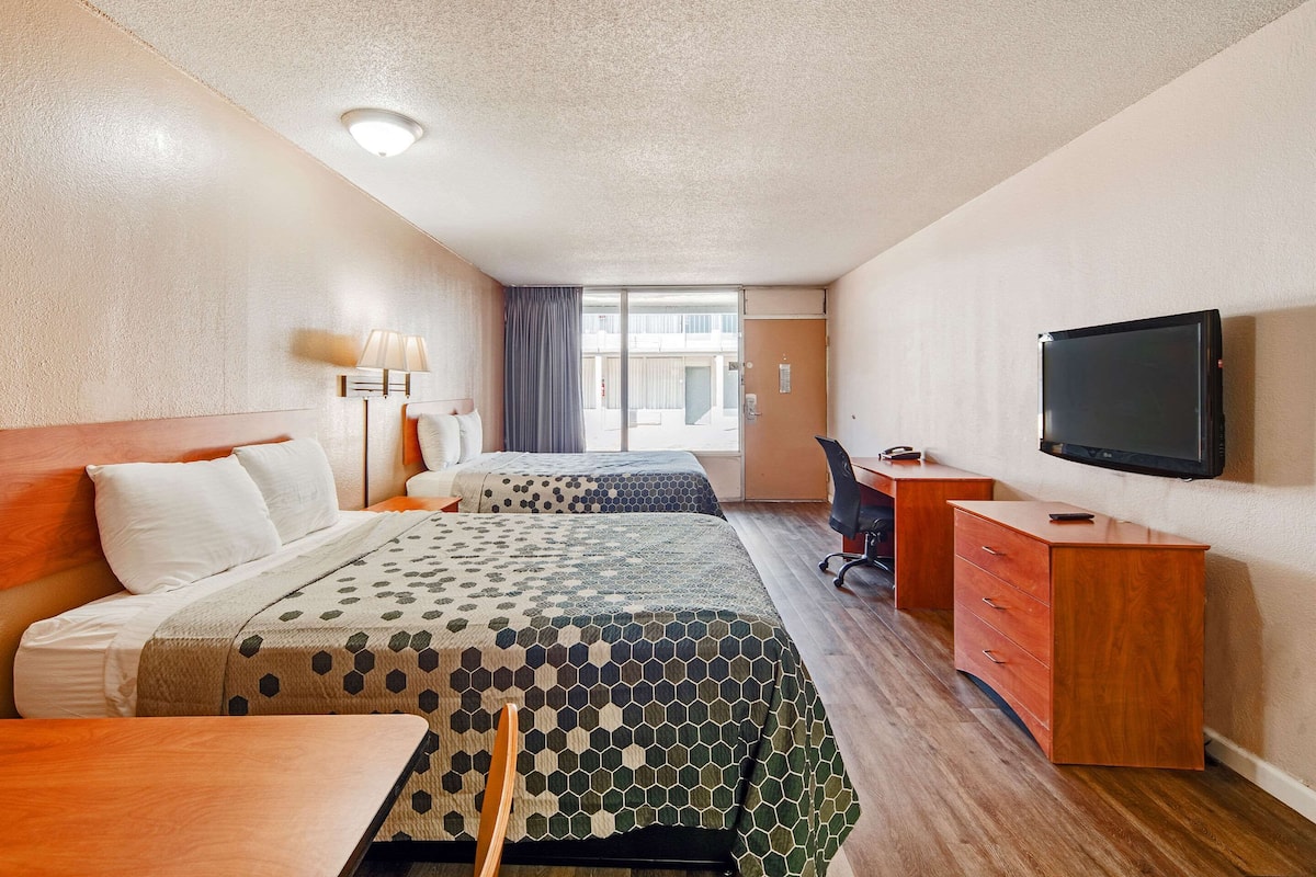 Habitación de hotel con dos camas, un escritorio, una silla, un televisor y una ventana con vistas al exterior.