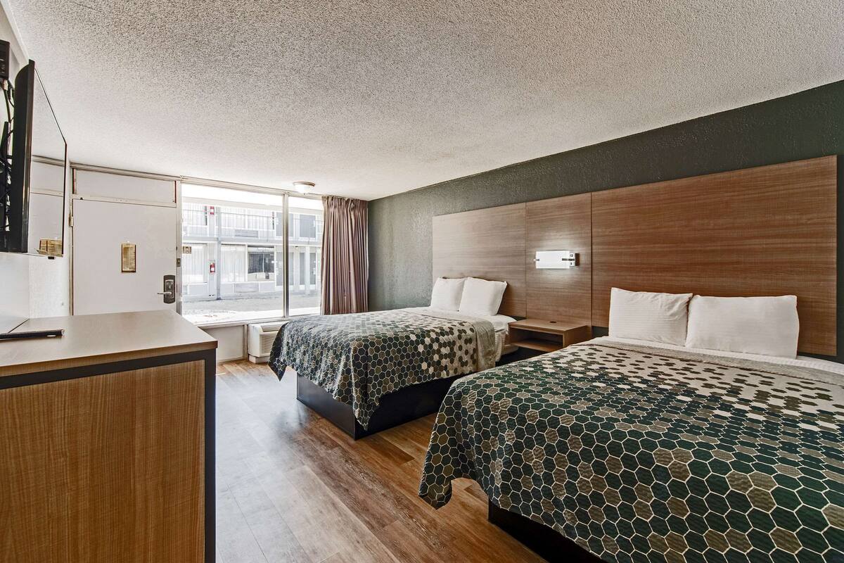 Habitación de hotel con dos camas, un escritorio y un ventanal grande.