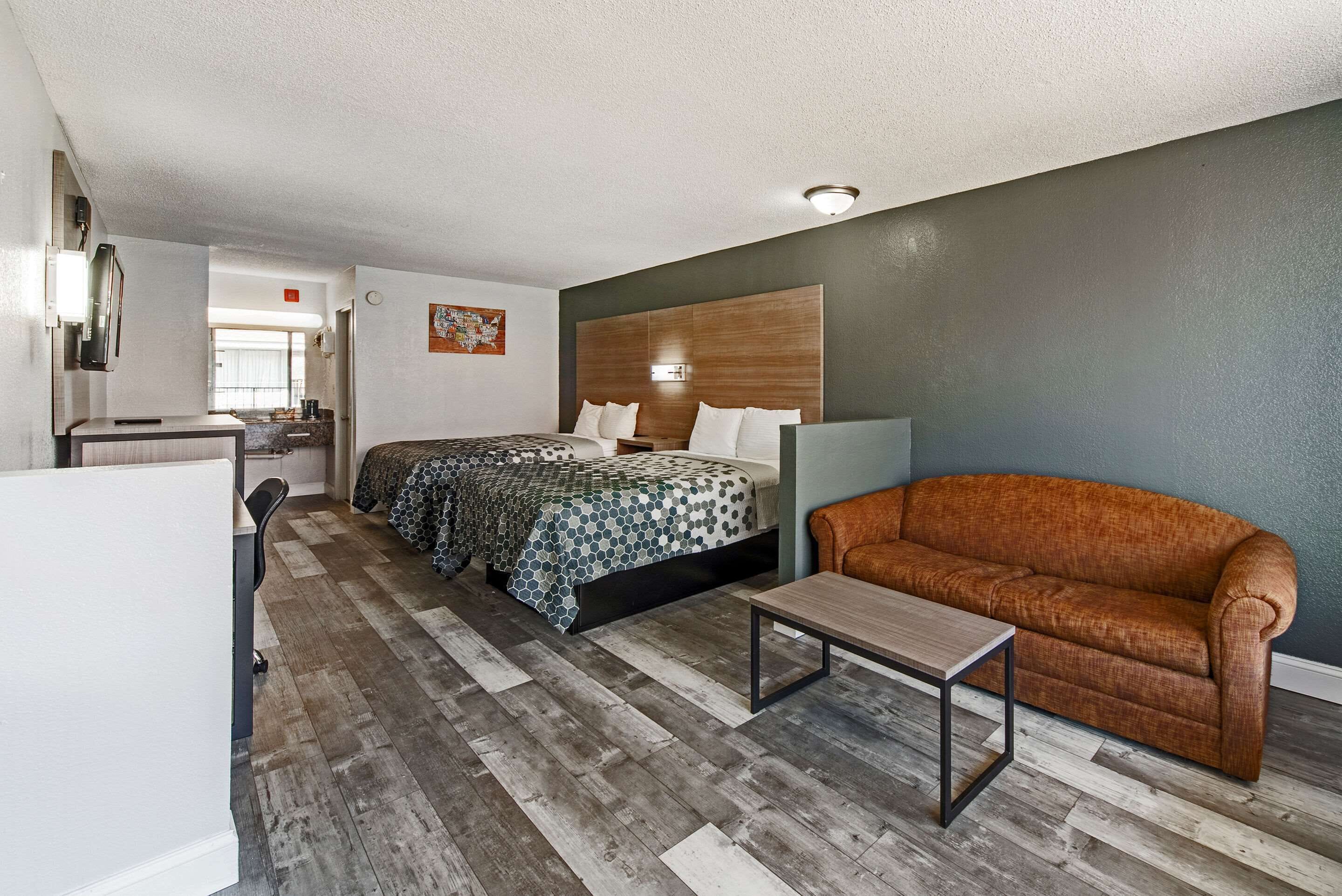A hotel room with two beds, a sofa, a small table, and a desk with a chair.
