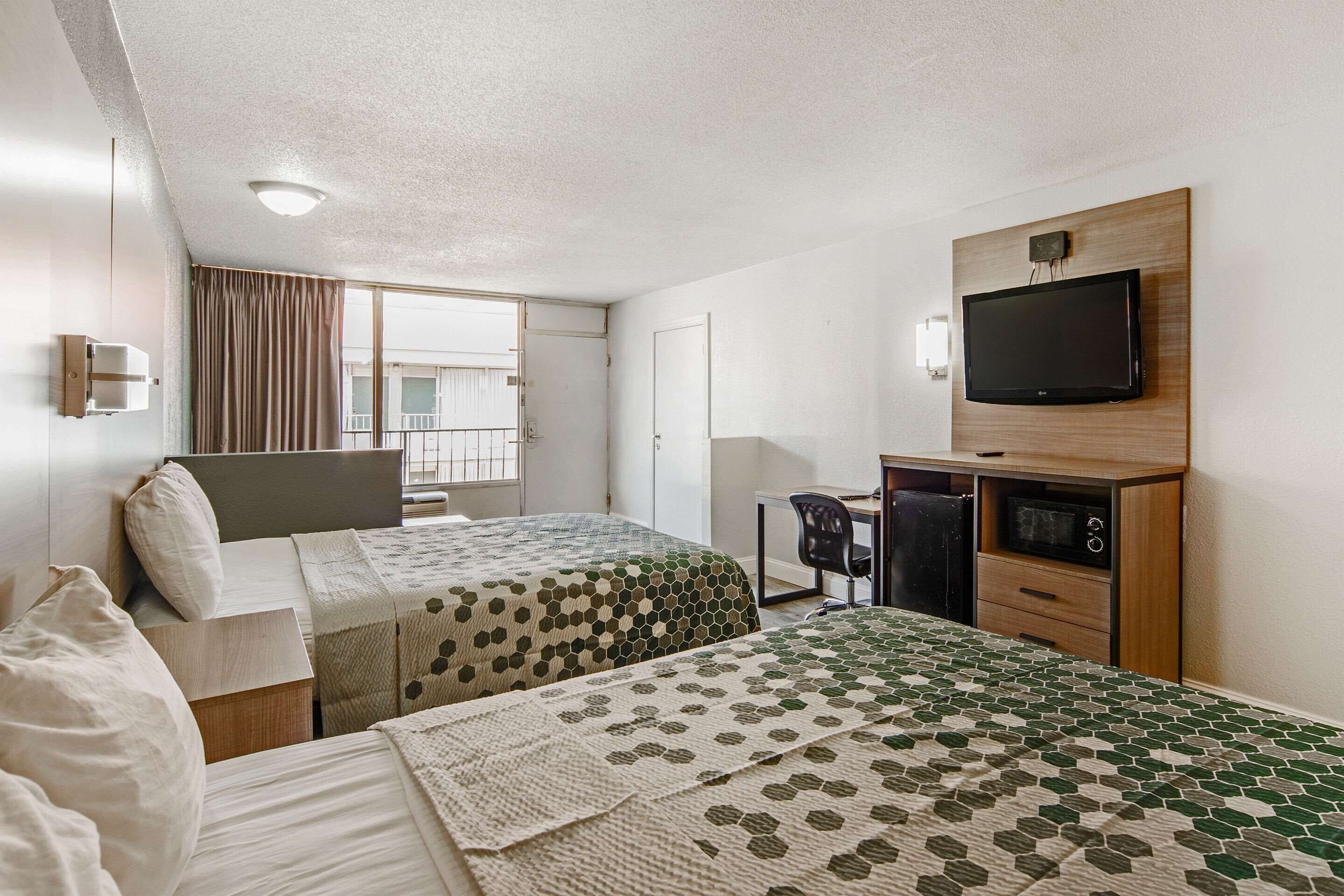 A hotel room with two beds, a desk, a chair, a television, and a window with curtains.
