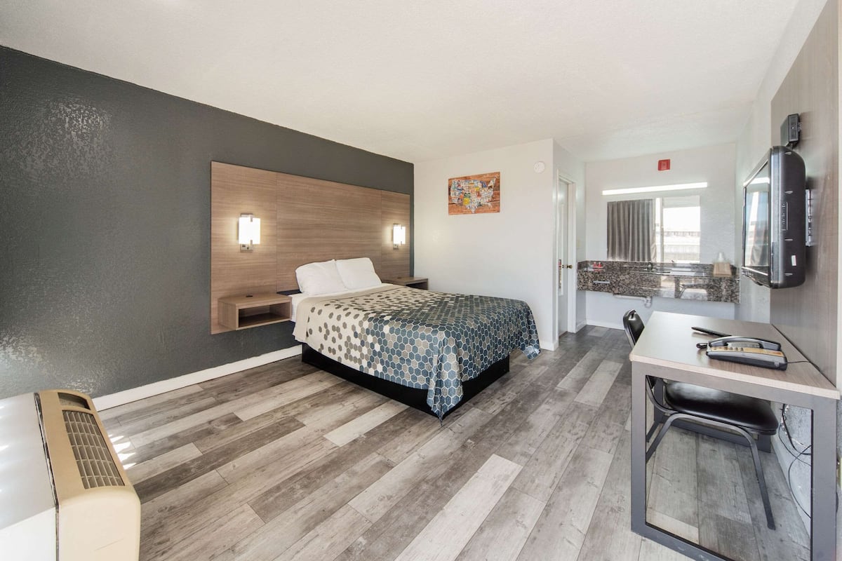 Una habitación de hotel con cama, mesita de noche, escritorio, silla y televisor.