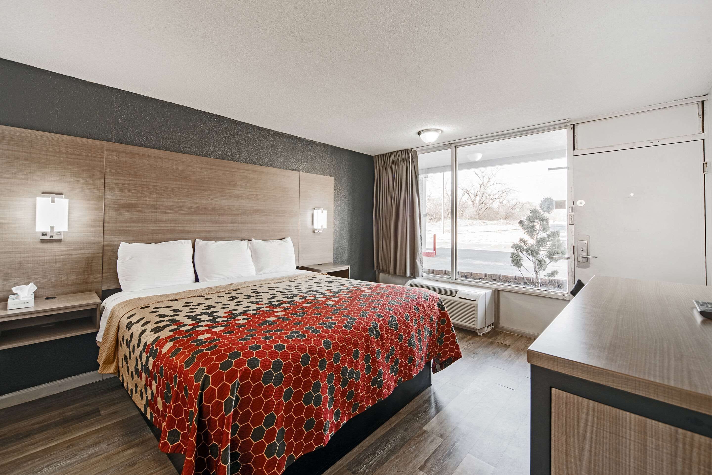 A hotel room with a bed, bedside tables, a desk, and a window with curtains.