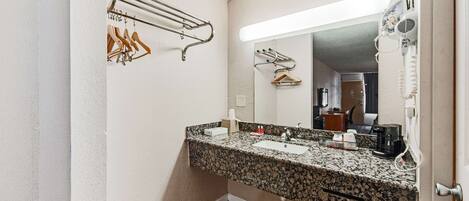 Une salle de bain avec un lavabo doté d’un plan de travail en granit, un miroir, un porte-serviettes et un sèche-cheveux.
