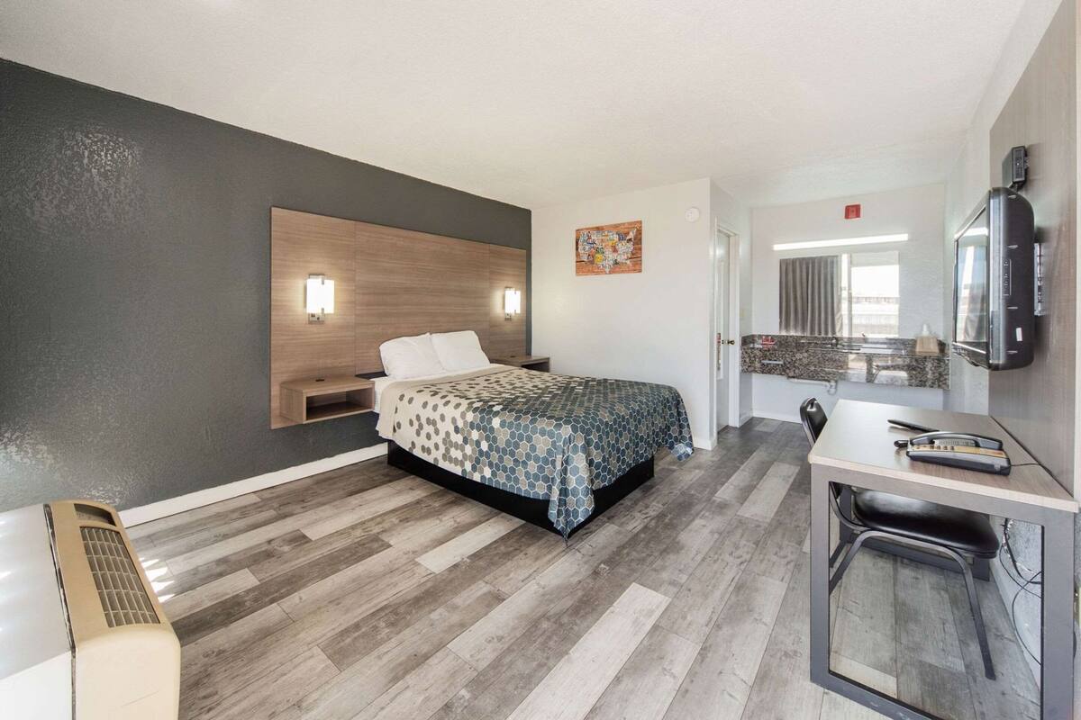 Una habitación de hotel moderna con cama, mesitas de noche, escritorio y microondas.