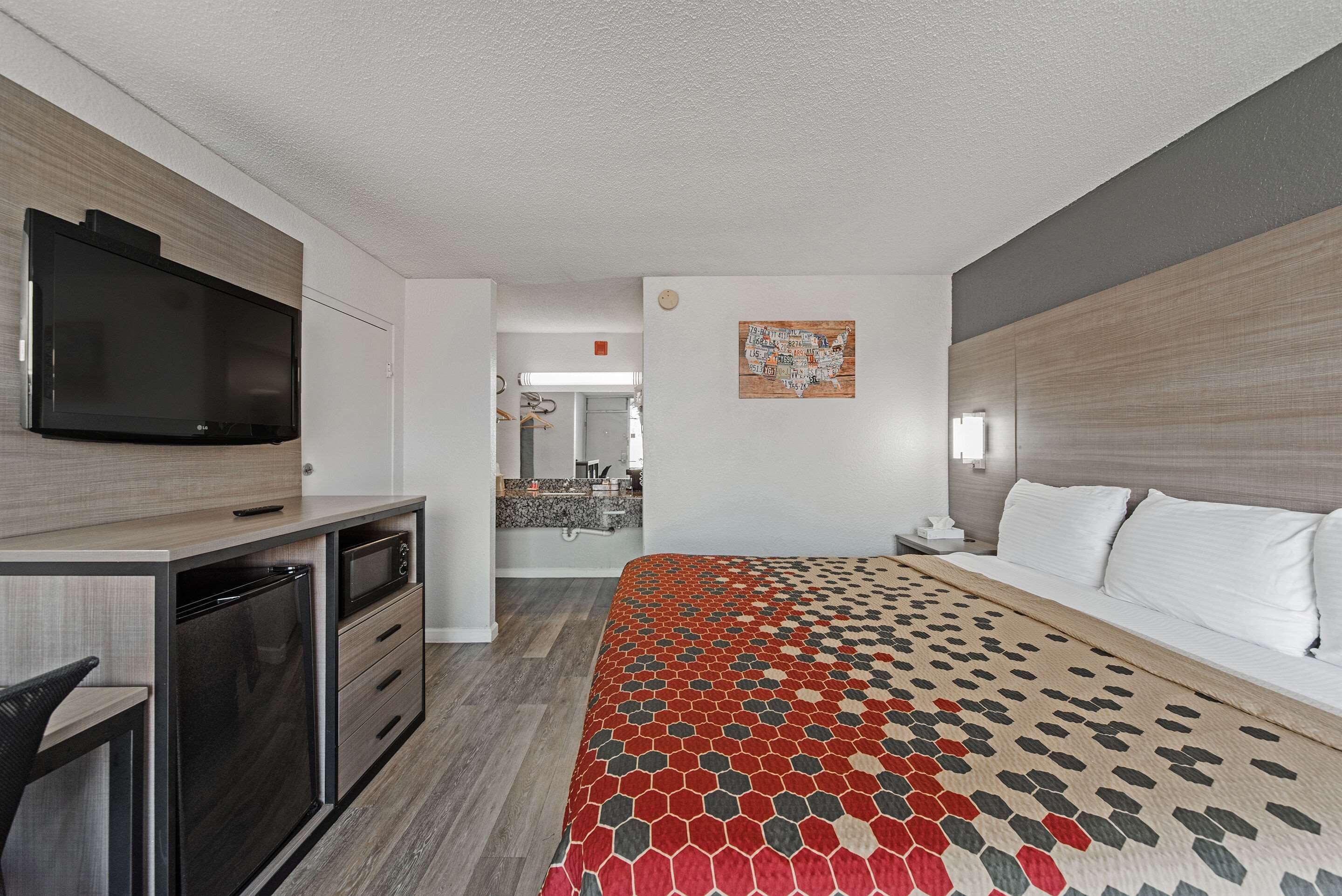 A hotel room with a bed, a desk with a television, a microwave, and a small kitchenette.