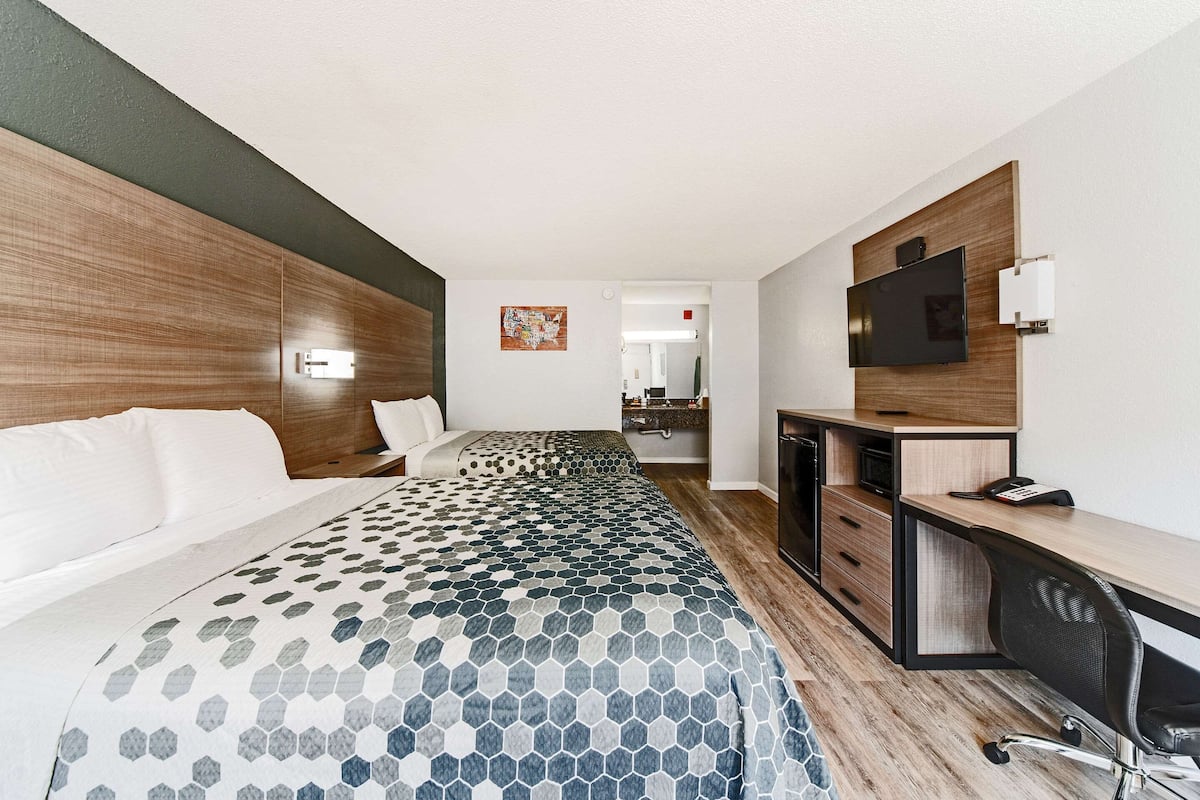 Habitación de hotel con cama, escritorio, silla, televisor y baño a la vista.