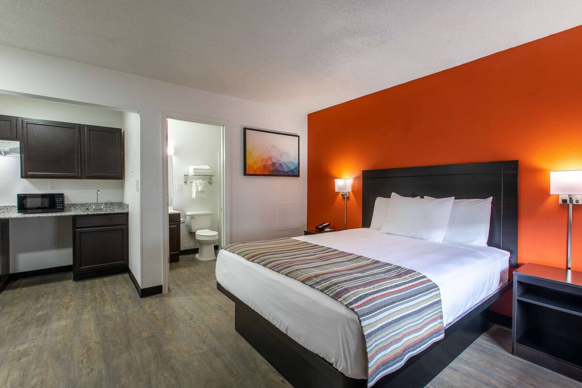 A hotel room with a bed, bedside table, and a desk with a microwave.