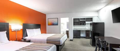 Habitación de hotel con dos camas, un escritorio y una kitchenette.