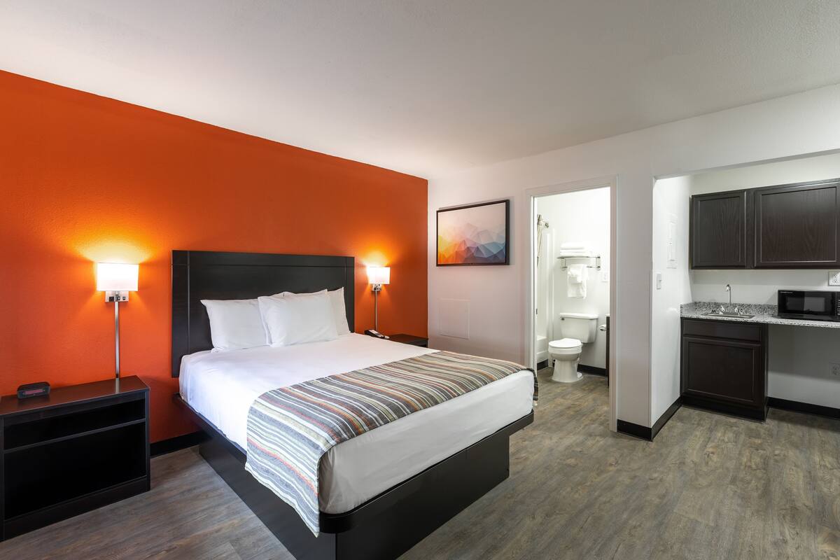 A hotel room with a bed, bedside tables, a nightstand, a bathroom, and a kitchenette.