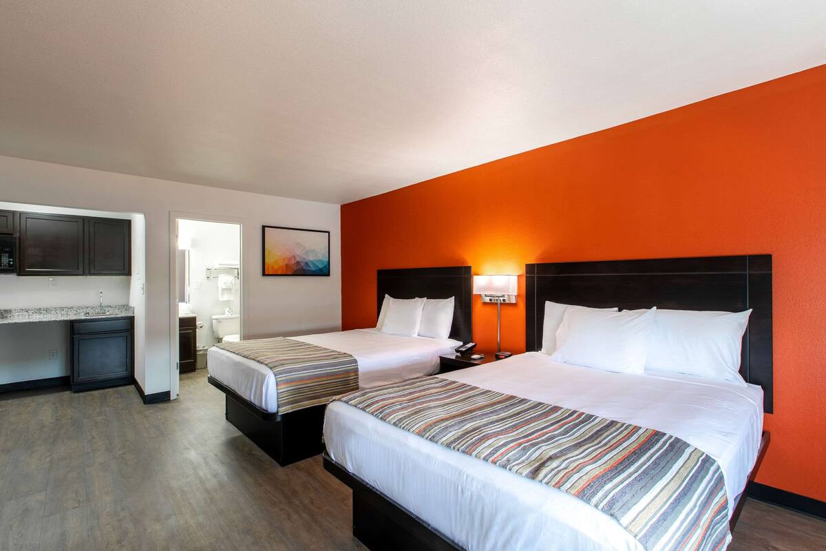 A hotel room with two beds, a kitchenette, and an orange accent wall.