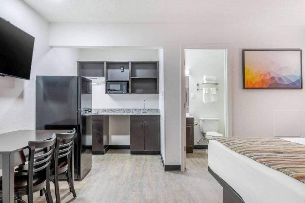 A compact hotel room with a kitchenette, a bed, a TV, and a bathroom.