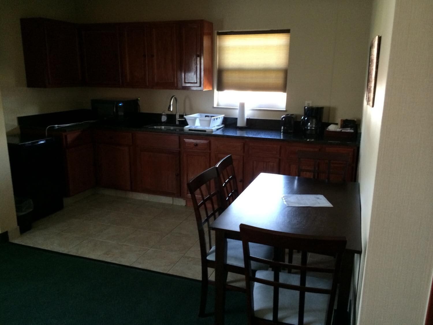 A compact kitchen with wooden cabinets, a sink, and a window with blinds.