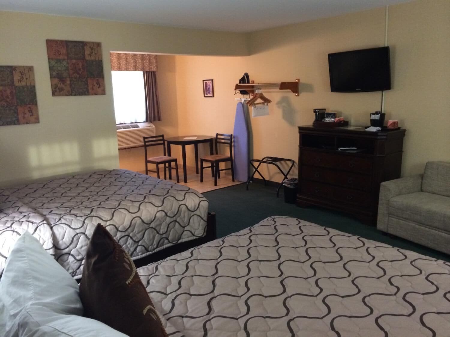 Quarto de hotel com duas camas, uma escrivaninha, uma cadeira, uma televisão e uma cômoda.