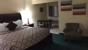 Ein Hotelzimmer mit einem großen Bett, einem Sessel, einem kleinen Tisch und zwei Bildern an der Wand.