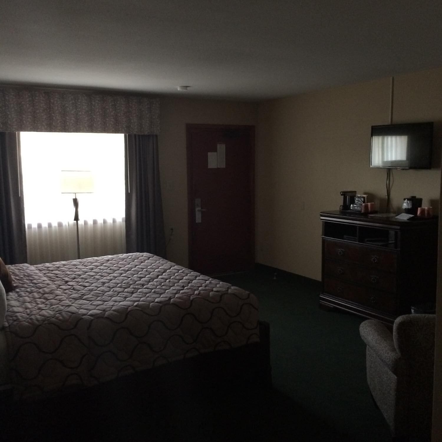 Una habitación de hotel con una cama, una cómoda, un televisor y una ventana con cortinas.