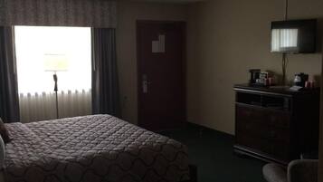 Una habitación de hotel con una cama, una cómoda, un televisor y una ventana con cortinas.