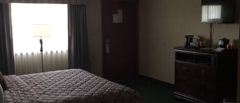 Una habitación de hotel con una cama, una cómoda, un televisor y una ventana con cortinas.