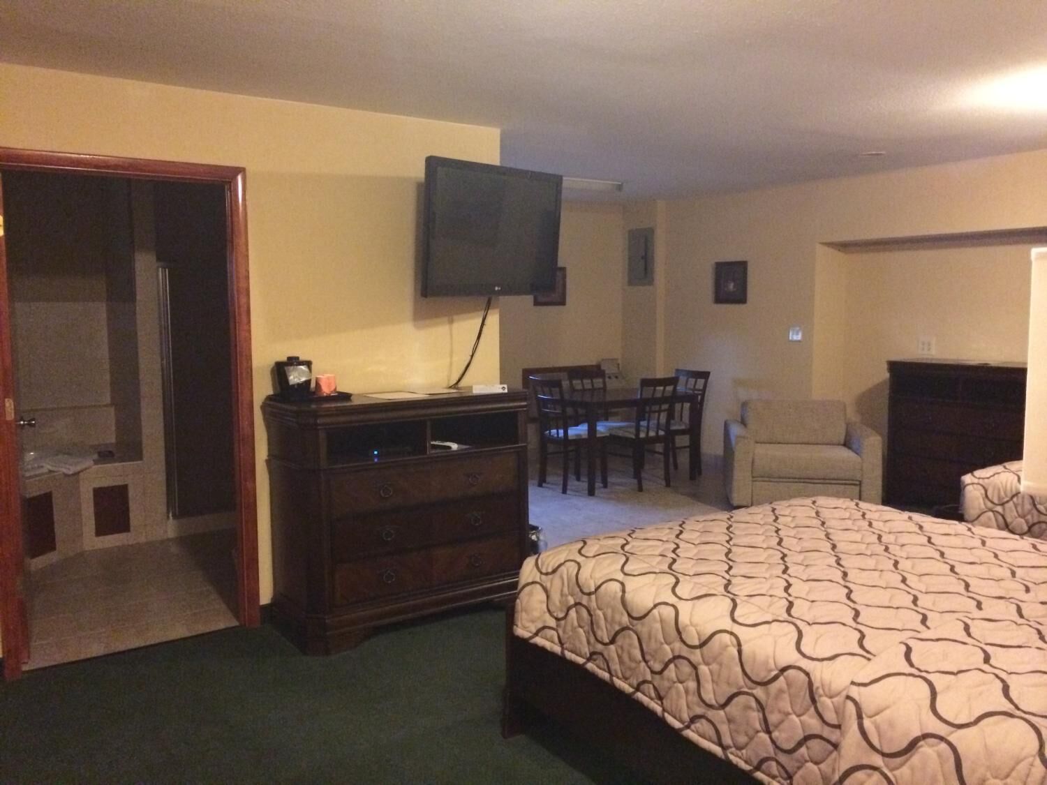 Un dormitorio con cama, cómoda, televisor montado en la pared, silla y escritorio.