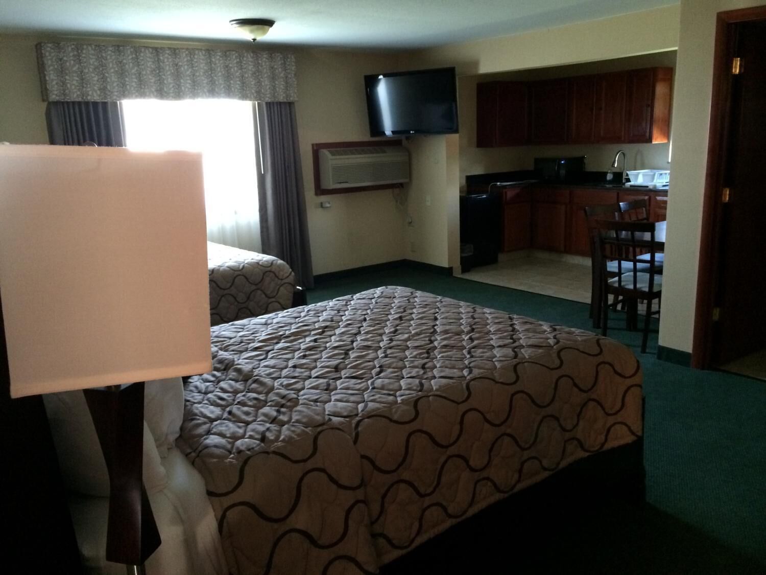 A hotel room with a bed, a desk, a chair, a television, and a kitchenette.