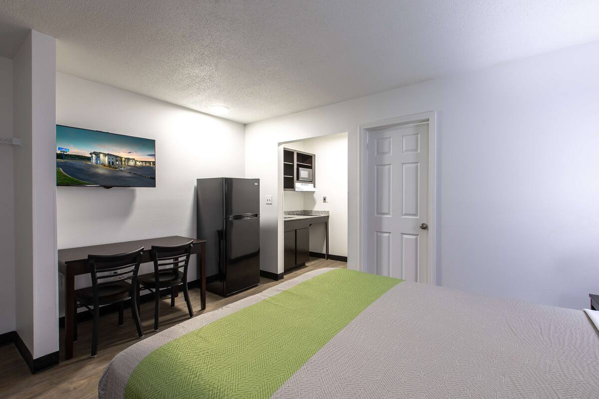 A hotel room with a bed, a desk with chairs, a refrigerator, a microwave, and a door.
