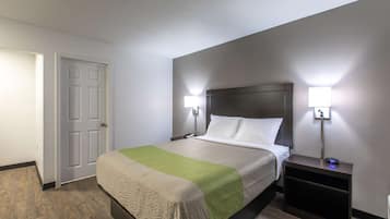 A neatly made bed with a green and beige blanket, two bedside lamps, and a nightstand with a clock.