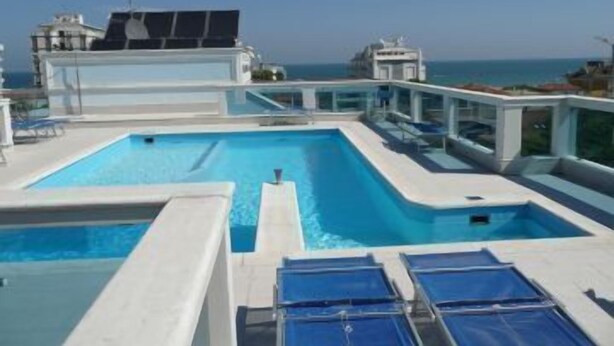 Zona de piscina con agua cristalina, tumbonas y vistas al mar.