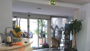 Zona de recepción con un mostrador de madera curvada, una planta en maceta y una silla.