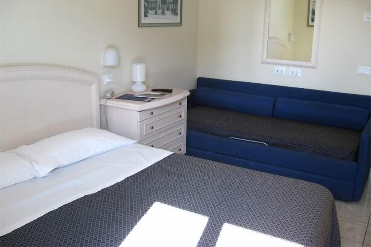 Une chambre à coucher avec un lit, une commode, une table de chevet avec une lampe, un canapé bleu et un tableau encadré au mur.