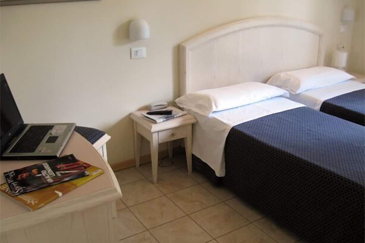 Une chambre d’hôtel avec un lit, une table de chevet sur laquelle se trouvent un ordinateur portable, un magazine et une lampe.