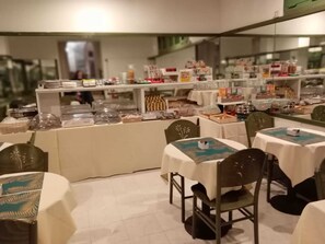 Un restaurant avec des tables et des chaises rondes, un espace buffet proposant divers plats, et un comptoir où sont présentés différents mets.