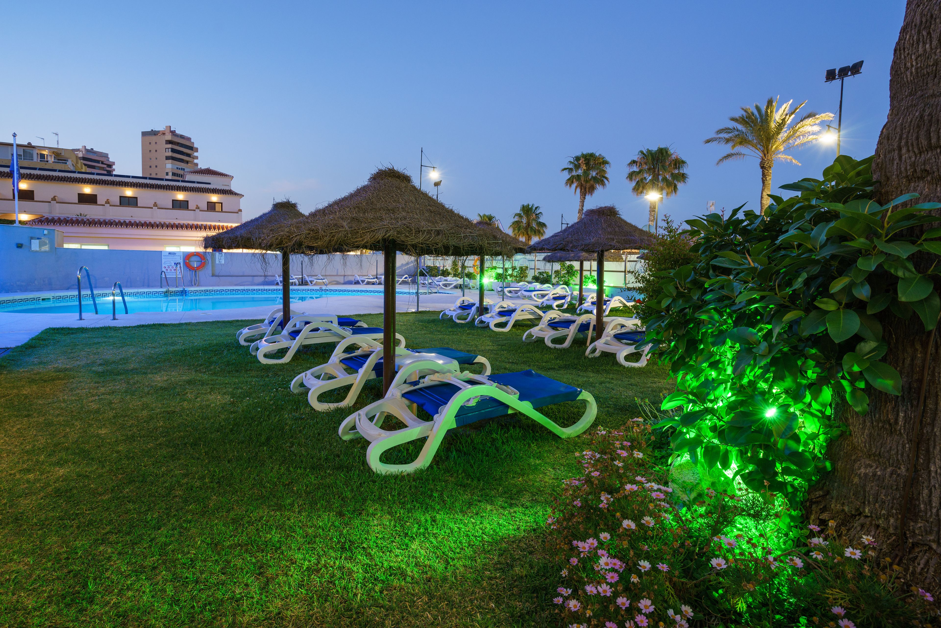 A poolside area with lounge chairs and umbrellas, a swimming pool, and a building in the background.