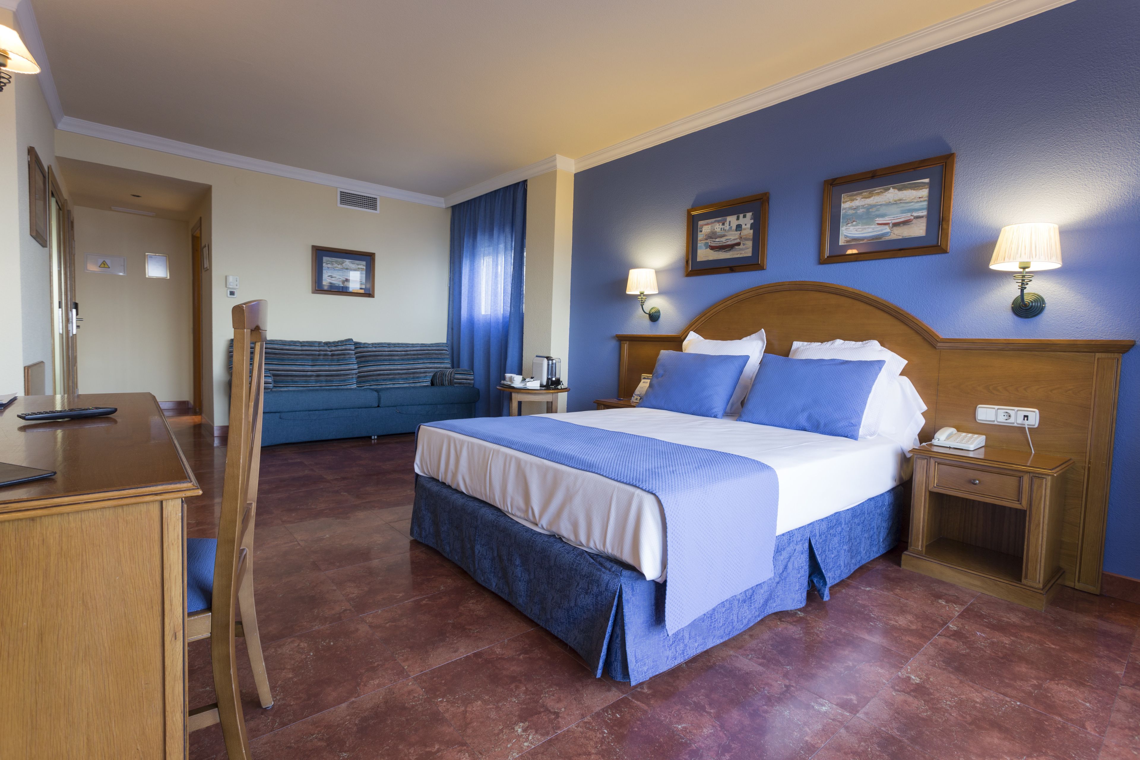 A hotel room with a large bed, a desk, and a chair. There are two bedside tables with lamps and a small table with a chair.