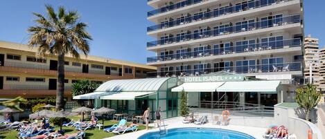 A hotel with a swimming pool, sun loungers, and palm trees.