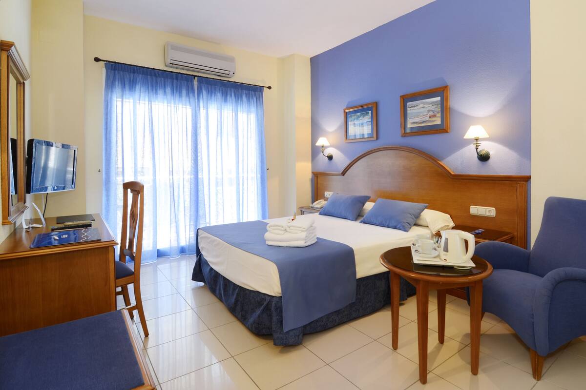 A hotel room with a bed, a desk, a chair, a television, and a window with curtains.