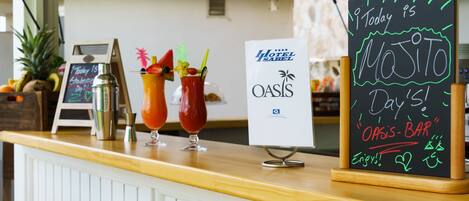 A bar area with a chalkboard sign announcing 'Today is Mojito Day' at Oasis Bar, featuring two cocktails and a sign for Hotel Oasis.