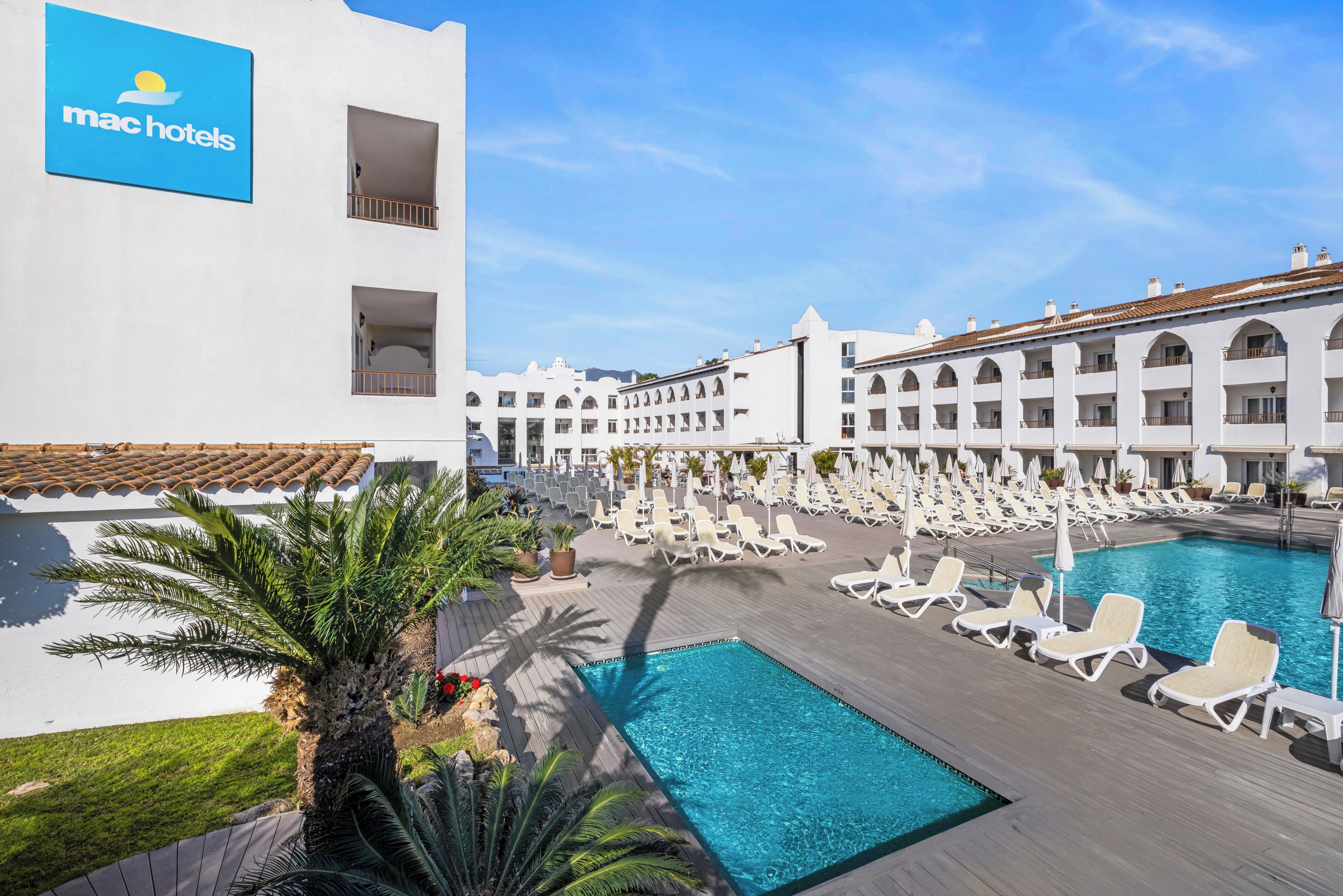 Een zwembad met ligbedden, een palmboom en een gebouw met een bordje 'mac hotels'.
