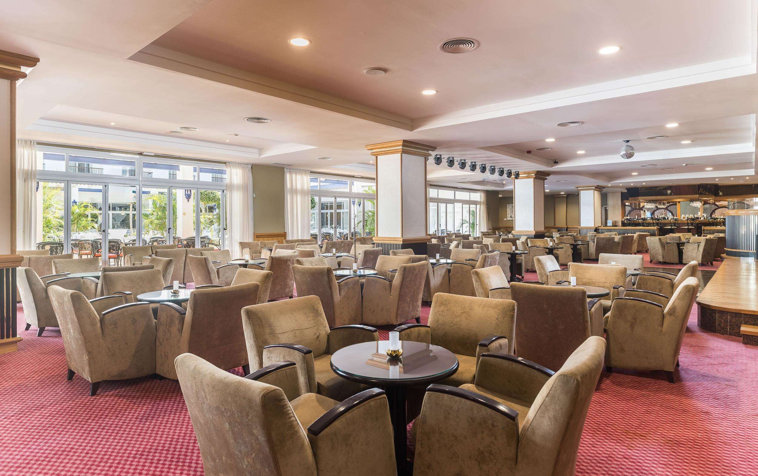 A spacious hotel lobby with multiple seating areas, large windows, and a bar area.