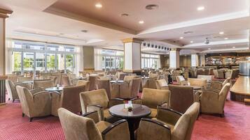 A spacious hotel lobby with multiple seating areas, large windows, and a bar area.
