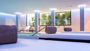 Une salle de spa moderne dotée d’une piscine, de chaises longues et d’une grande fenêtre offrant une vue sur un paysage tropical.