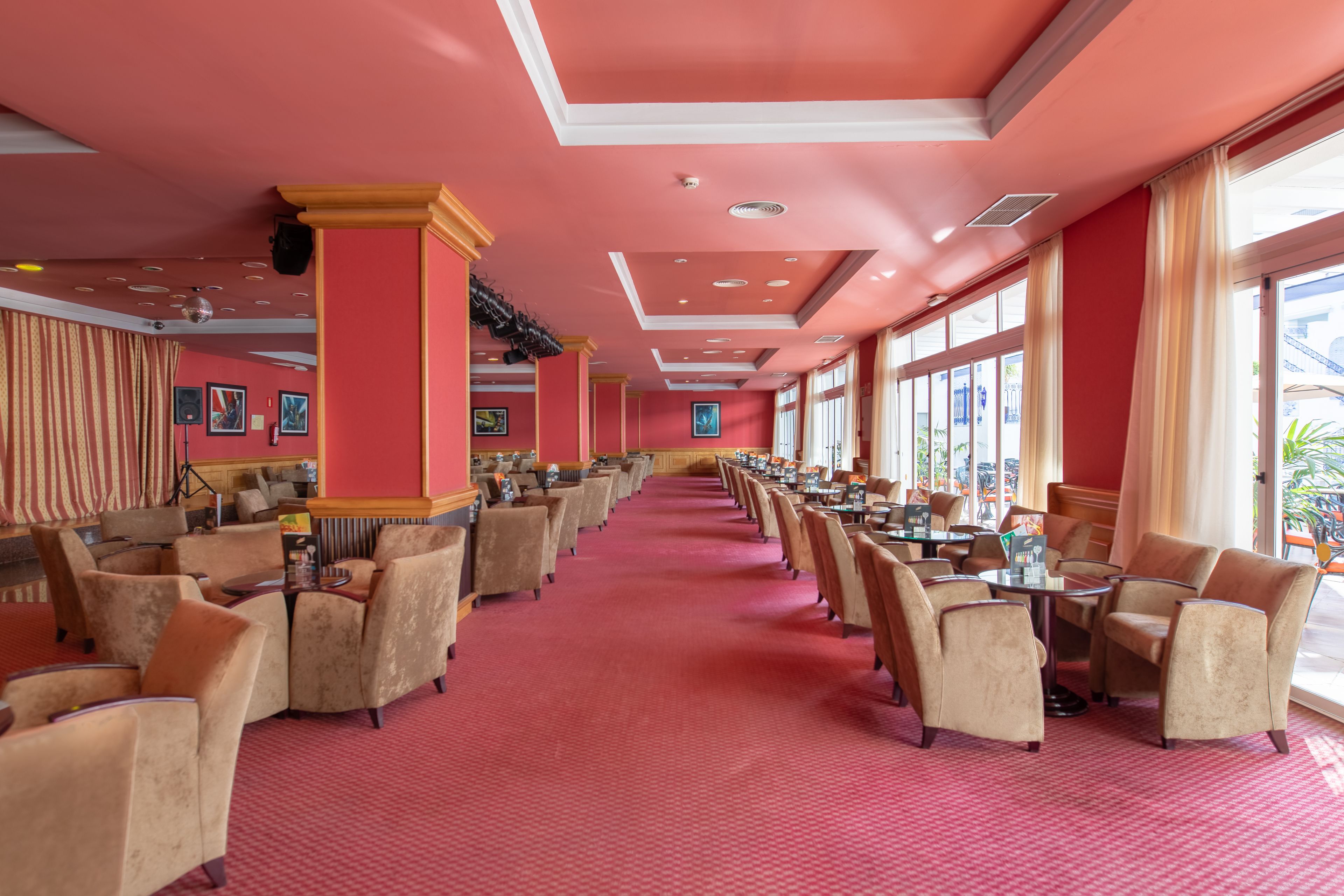 A spacious hotel lobby with a red carpet, multiple seating areas, and large windows offering views.