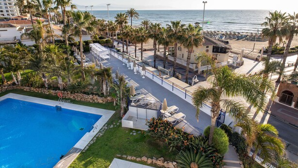 Un complexe hôtelier doté d’une piscine, de chaises longues, de palmiers et offrant une vue sur la plage et l’océan.