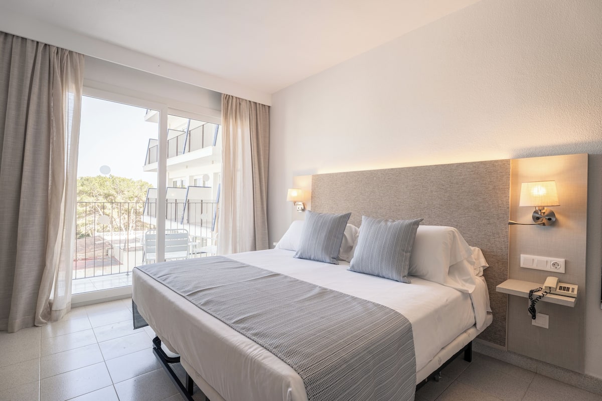 Une chambre d’hôtel avec un lit, une table de chevet avec une lampe, un téléphone et une vue sur l’extérieur.