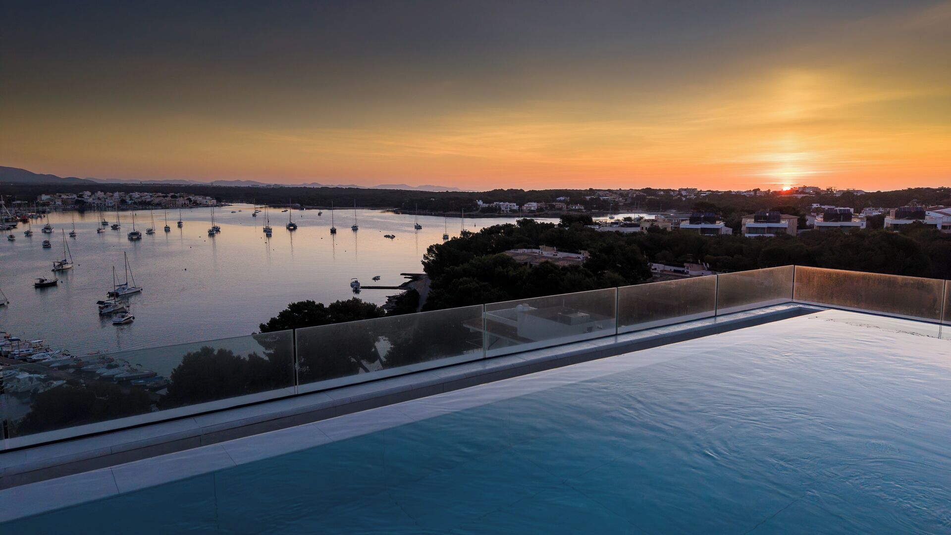 Una piscina en la azotea con vistas a un puerto deportivo al atardecer.