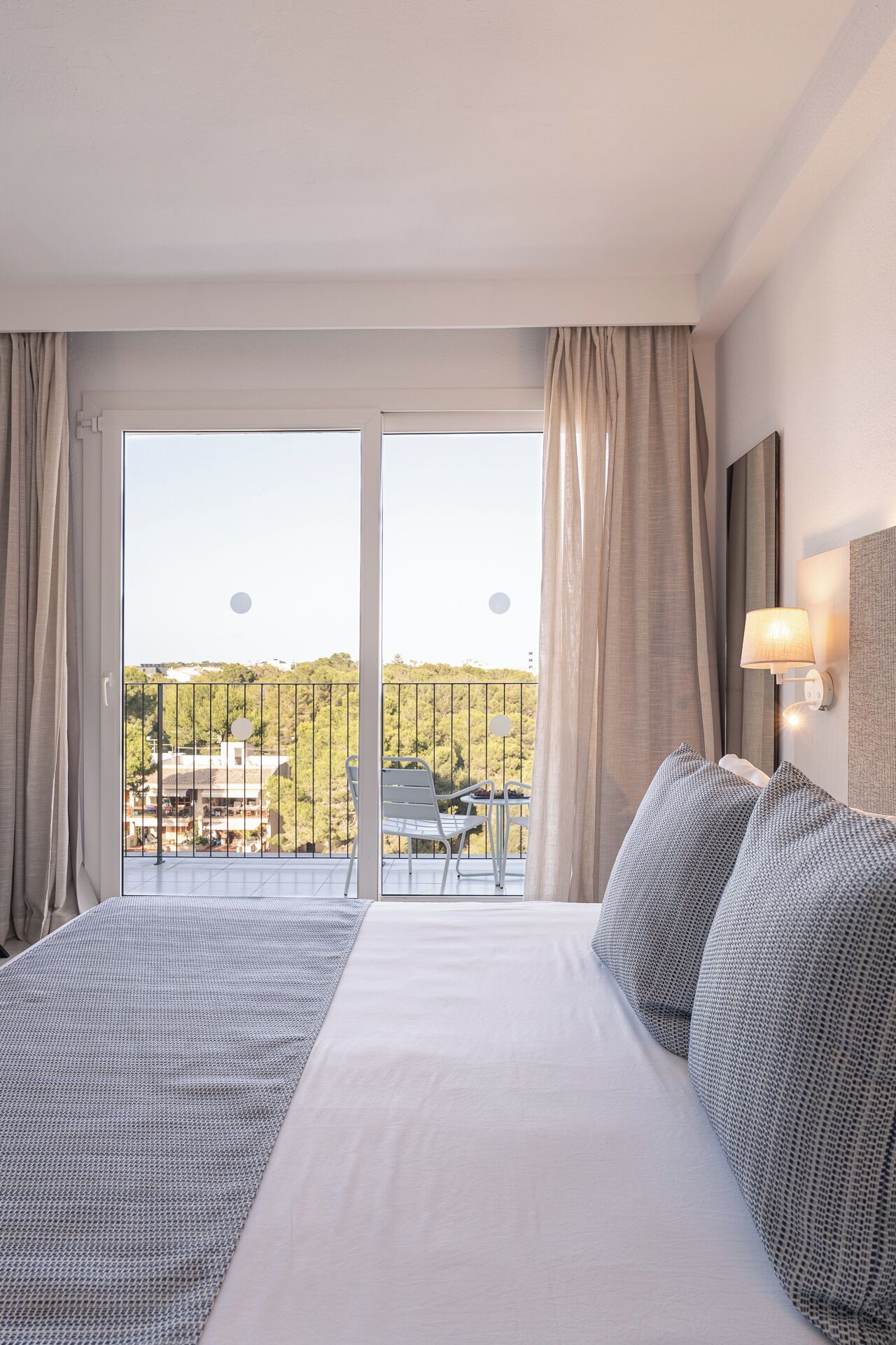 Habitació d'hotel amb un llit, un balcó amb taula i cadires, i vista a la ciutat.