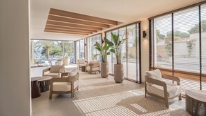Un intérieur moderne avec de grandes fenêtres, un coin salon avec des fauteuils et une table, et des plantes en pot.