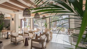 Un espace intérieur spacieux avec des meubles en osier, des luminaires suspendus et de grandes fenêtres offrant une vue sur l’extérieur.