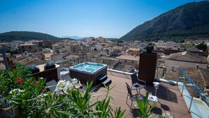 A rooftop terrace with a hot tub, outdoor seating, and a view of a town with buildings and hills in the background. - Hotel Juma (Pollenca)