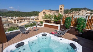 A rooftop terrace with a hot tub, lounge chairs, and a view of a historic church and mountains. - Hotel Juma (Pollenca)