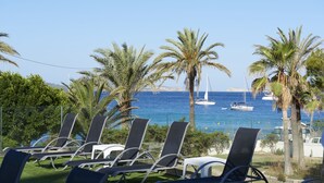 A beachside view with lounge chairs, palm trees, and boats on the water. - Hotel Abrat (Sant Antoni de Portmany)
