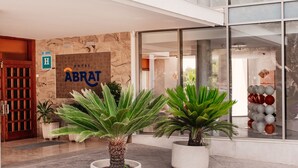 A modern hotel entrance with a sign reading "ABRAT HOTEL," large glass windows, and potted plants in the foreground. - Hotel Abrat (Sant Antoni de Portmany)
